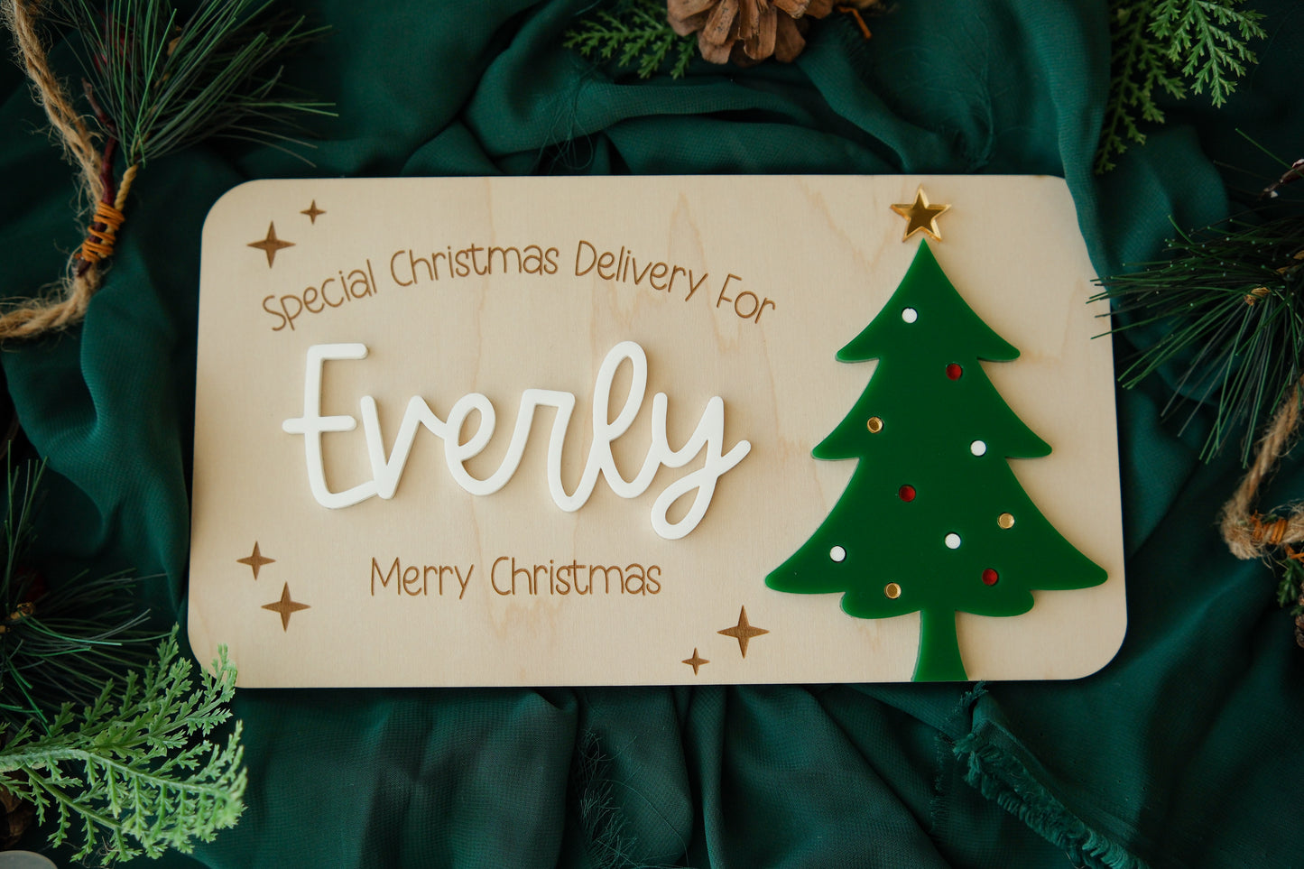 Wooden sign with 'Special Christmas Delivery For Everly' and a Christmas tree on a green fabric background.