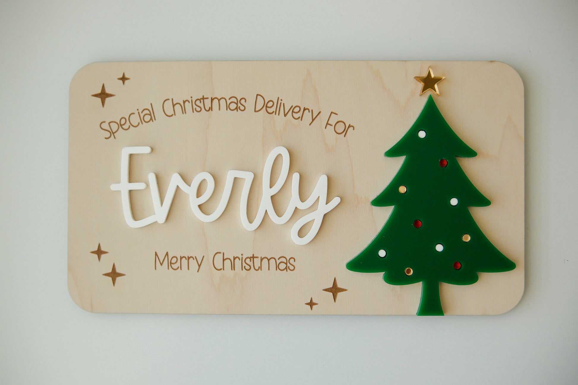 Wooden plaque with 'special Christmas Delivery for Everly' text and a green Christmas tree design on a light background.