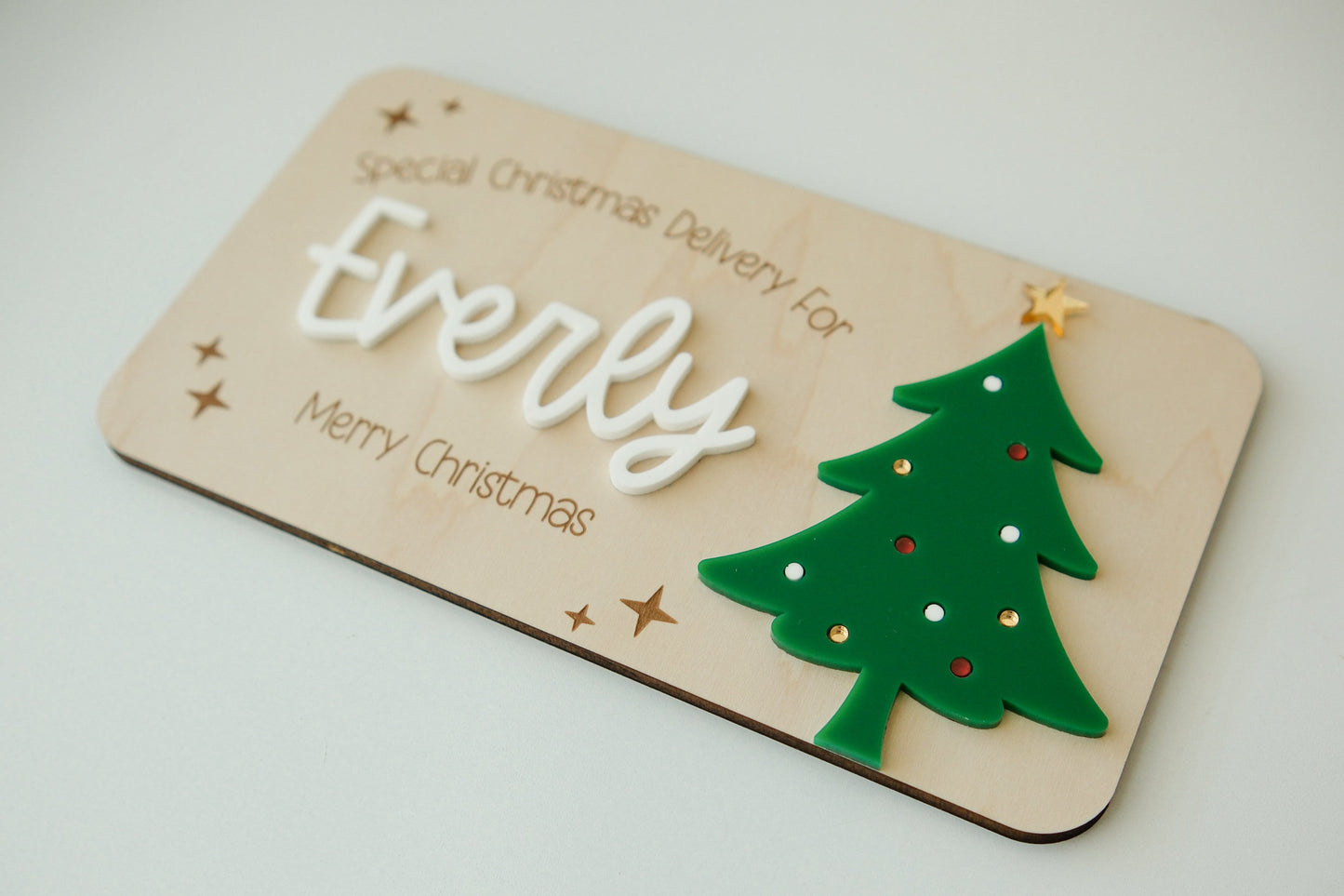Wooden plaque with 'special Christmas Delivery for Everly' text and a green Christmas tree design on a light background.